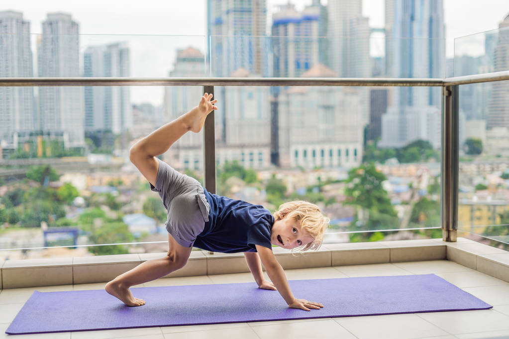 Щасливий хлопчик практикує йогу на своєму балконі з панорамним видом на велике місто
. - Фото, зображення