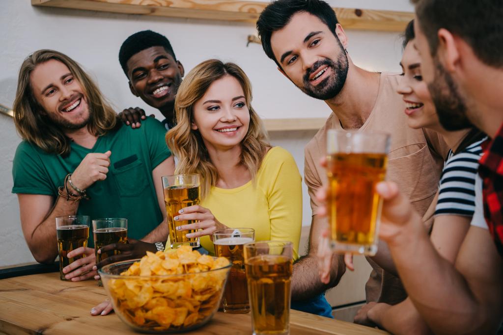 Happy πολυπολιτισμική φίλοι με μπύρα και chips παρακολουθώντας ποδόσφαιρο αγώνα και μιλώντας στο μπαρ  - Φωτογραφία, εικόνα