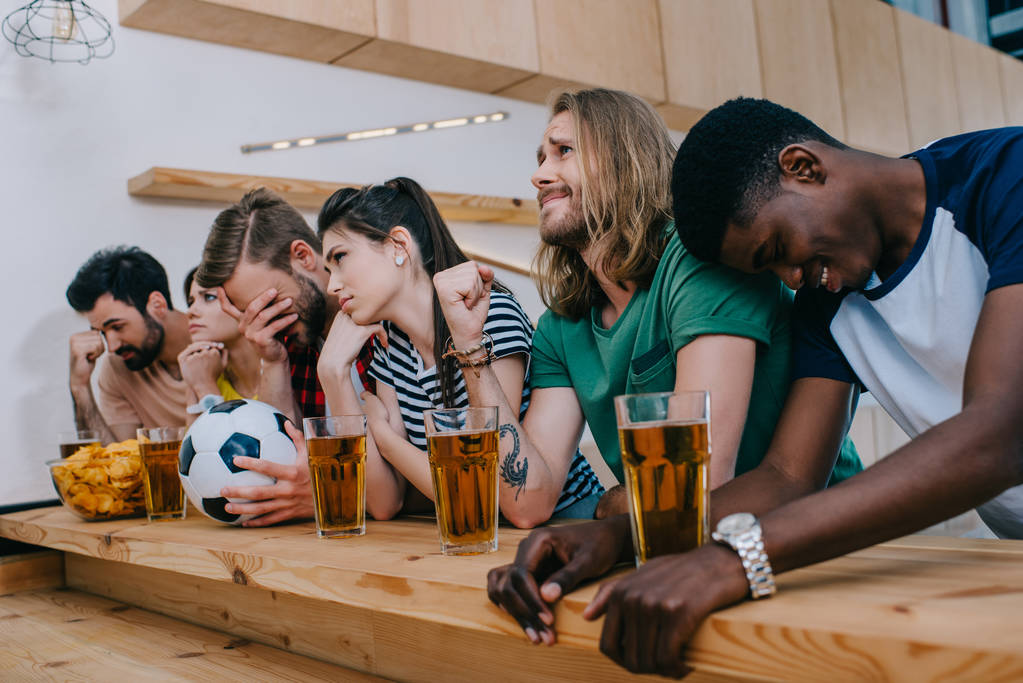 засмучена мультикультурна група друзів сидить за барною стійкою і дивиться футбольний матч
 - Фото, зображення