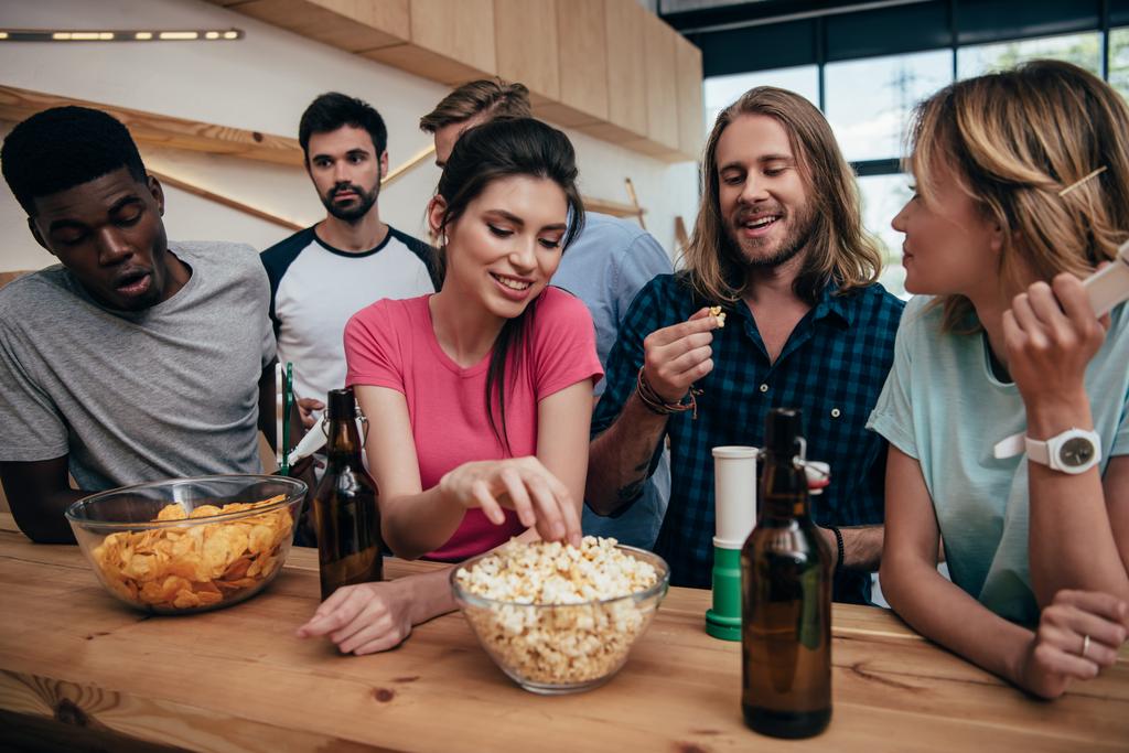 усміхнена багатоетнічна група друзів їсть попкорн і дивиться футбольний матч в барі
  - Фото, зображення