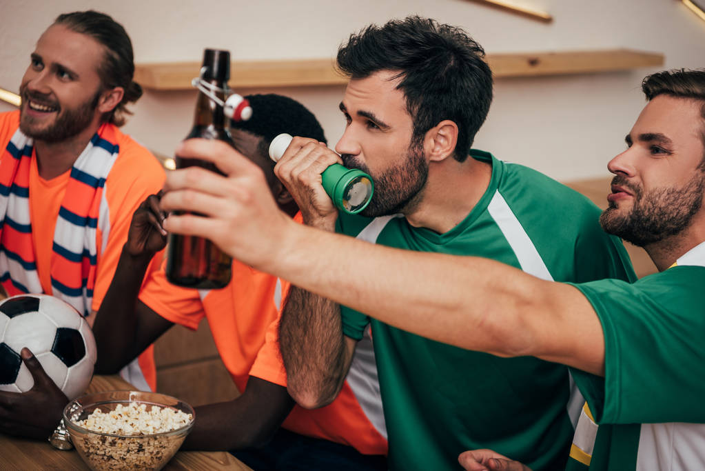 Grupa wielokulturowych kibiców w pomarańczowe i zielone koszulki oglądając mecz w piłkę nożną bar  - Zdjęcie, obraz