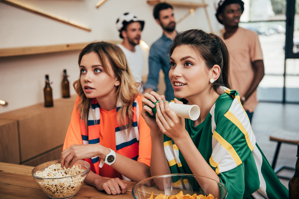 émotionnel jeunes amies dans différents ventilateur t-shirts et foulards regarder match de football au bar
  - Photo, image