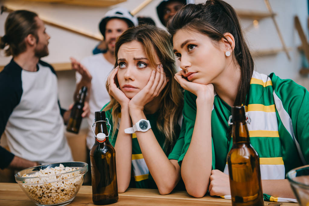 Aufgebrachte junge Frauen und ihre männlichen Freundinnen, die während des Fußballspiels an der Bar hinter ihnen stehen  - Foto, Bild