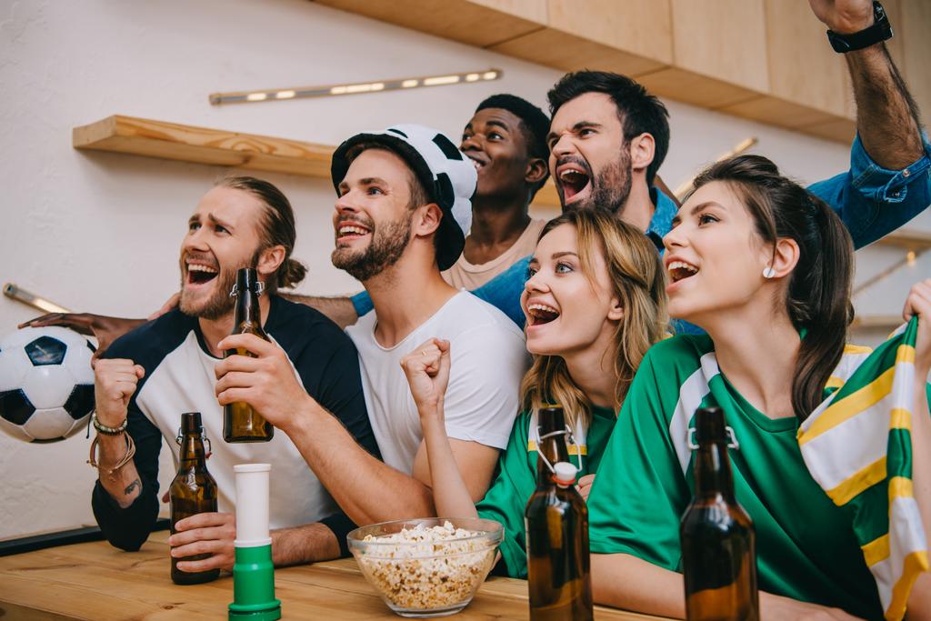aufgeregte multikulturelle Freunde mit Bierflaschen, die während des Fußballspiels an der Bar Ja-Gesten machen  - Foto, Bild