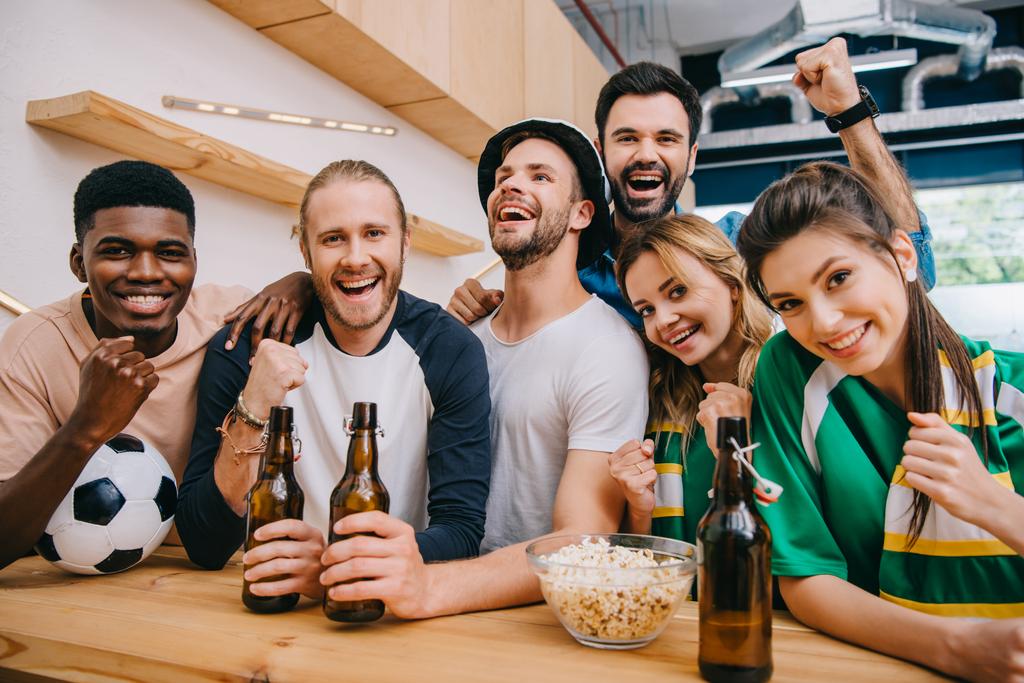щасливі багатокультурні друзі з пляшками пива святкують і роблять так жести під час спостереження за футбольним матчем в барі
  - Фото, зображення