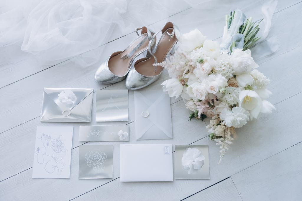 top view of stylish wedding invitations with bridal shoes and bouquet on wooden floor - Photo, Image