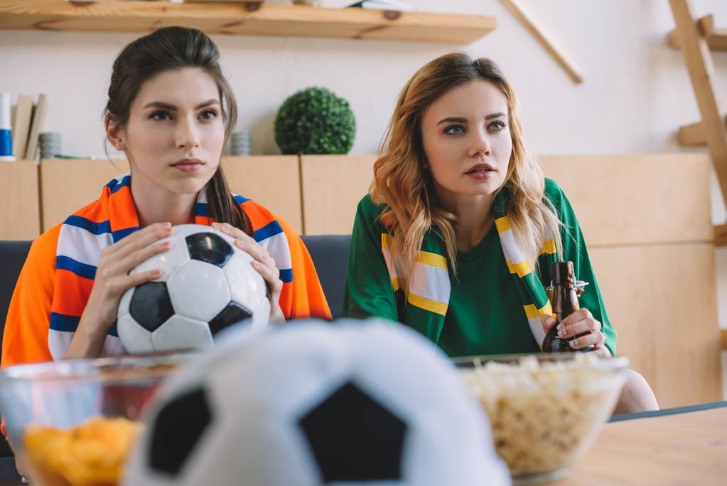 focada fãs de futebol feminino em diferentes t-shirt e scarfs assistindo jogo de futebol em casa
  - Foto, Imagem