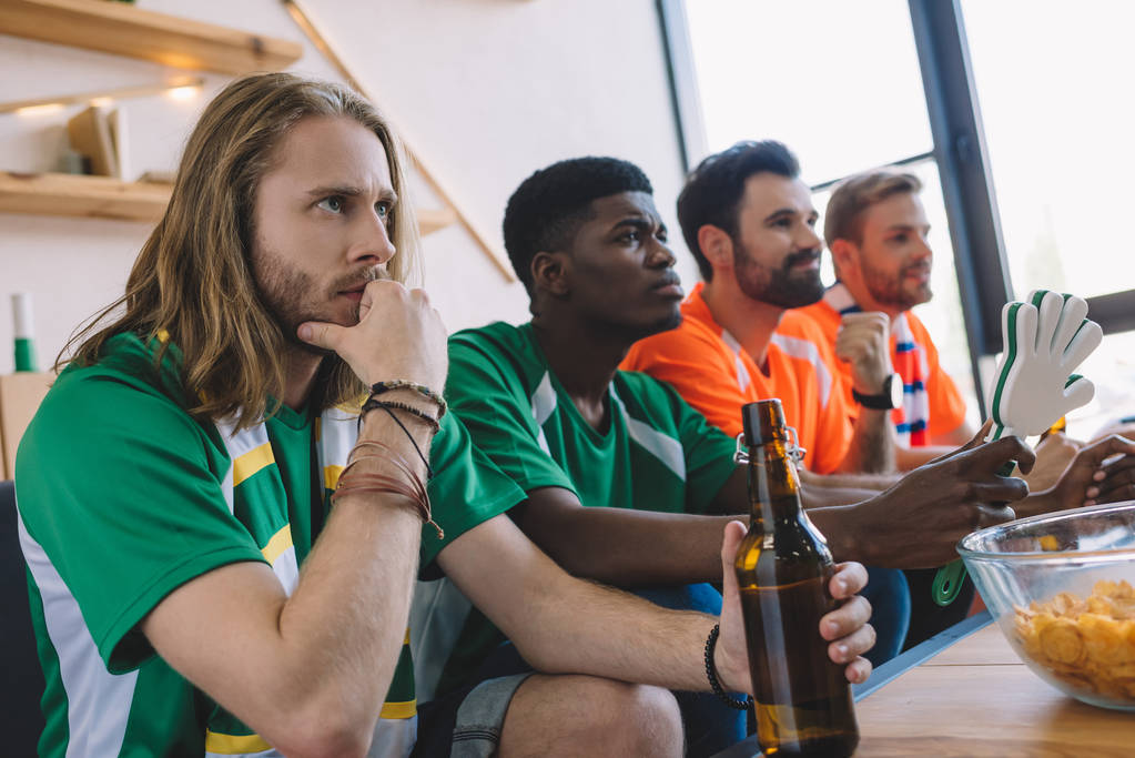 koncentruje się grupa przyjaciół płci męskiej wielokulturowym w różnych wentylator koszulki oglądanie piłka nożna mecz w domu - Zdjęcie, obraz