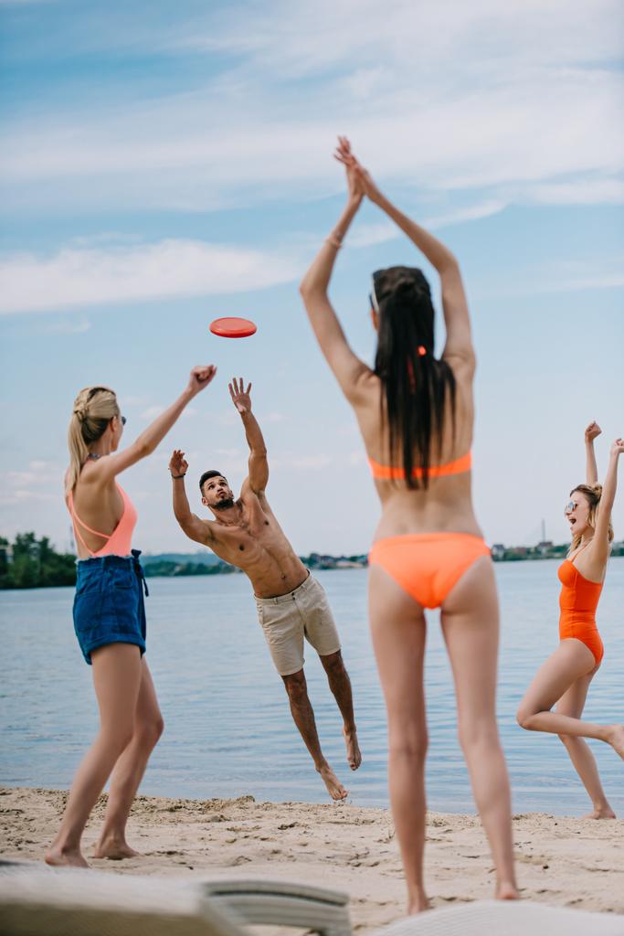 gelukkige jonge mensen die spelen met de frisbee op zandstrand - Foto, afbeelding