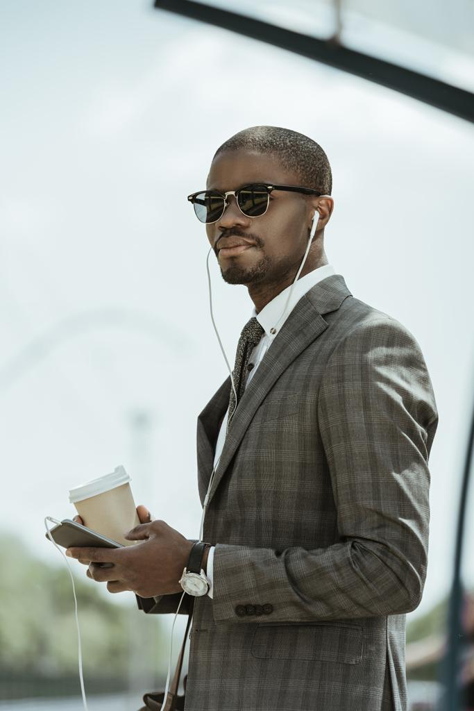 Jovem empresário afro-americano ouvindo música e segurando xícara de café na estação de transporte público
 - Foto, Imagem
