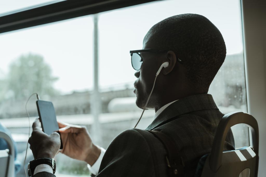 Stijlvolle vertrouwen zakenman in oortelefoons met smartphone terwijl het nemen van de trein - Foto, afbeelding