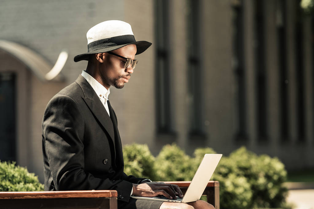 Elegante hombre con traje de trabajo en el ordenador portátil mientras está sentado en el banco
 - Foto, imagen
