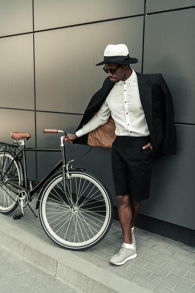 Homem elegante vestindo camisa branca e jaqueta em pé por sua bicicleta
 - Foto, Imagem