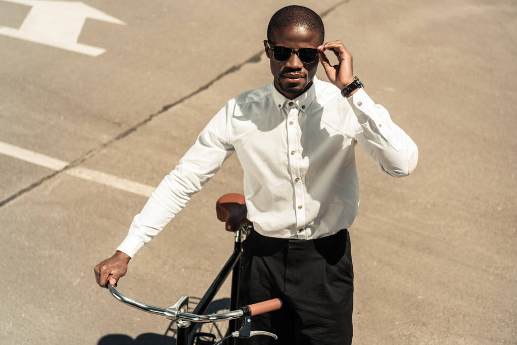 Stylish man wearing white shirt standing by his bicycle on street - Photo, Image