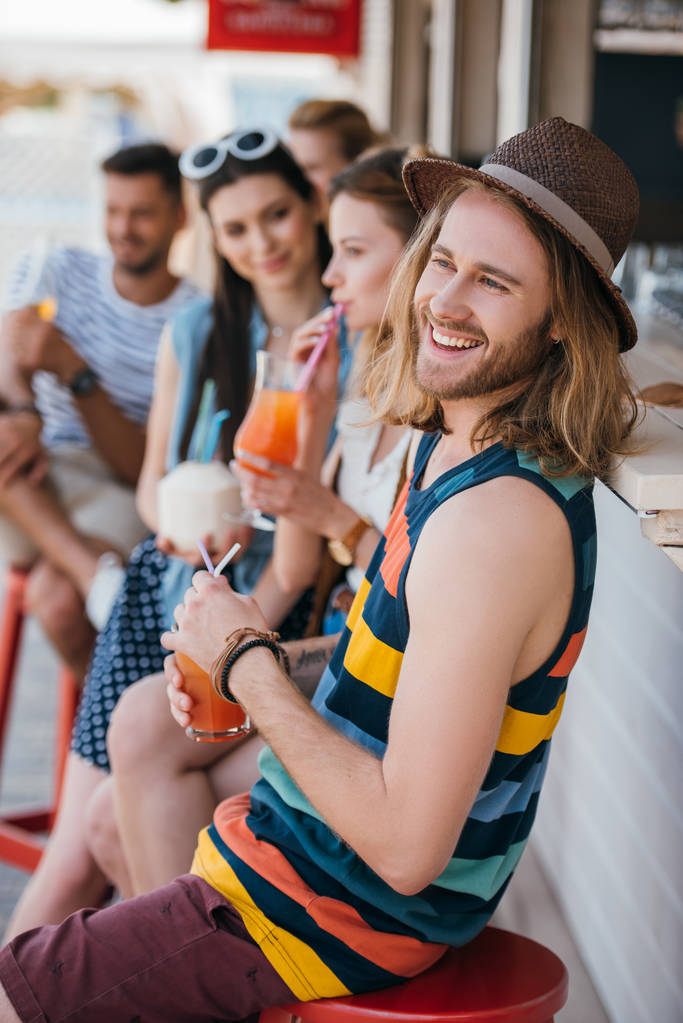 όμορφος νεαρός χαμογελαστός και πόσιμο καλοκαιρινό κοκτέιλ στο beach bar - Φωτογραφία, εικόνα