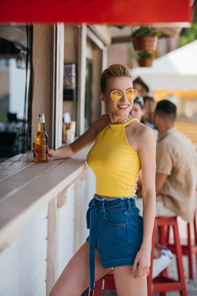 krásná usměvavá dívka drží sklenici piva v plážovém baru - Fotografie, Obrázek