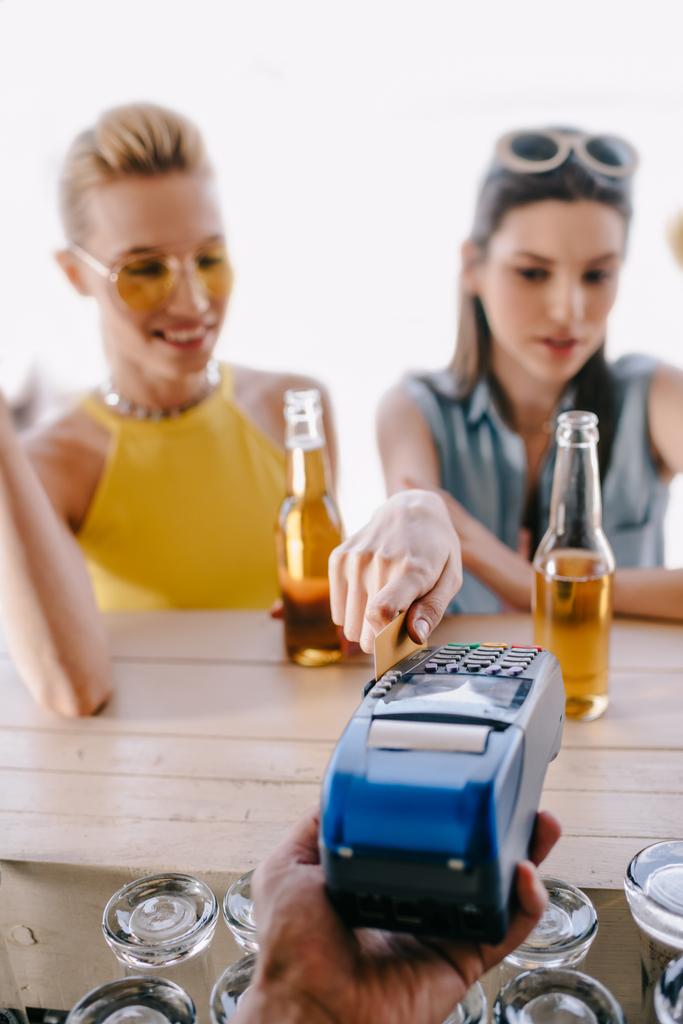 enfoque selectivo de las niñas que beben cerveza y pagan con tarjeta de crédito en la terminal en el bar de playa
 - Foto, imagen