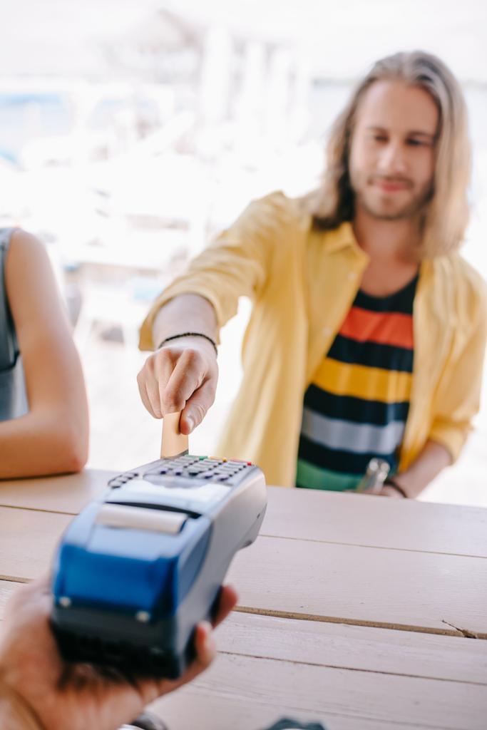 Selektywny fokus młody człowiek płatności kartą kredytową na terminalu w barze na plaży   - Zdjęcie, obraz
