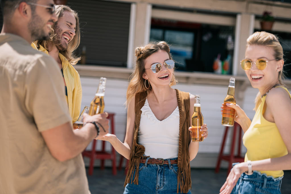 Lächelnde junge Leute trinken Bier und unterhalten sich an der Strandbar - Foto, Bild