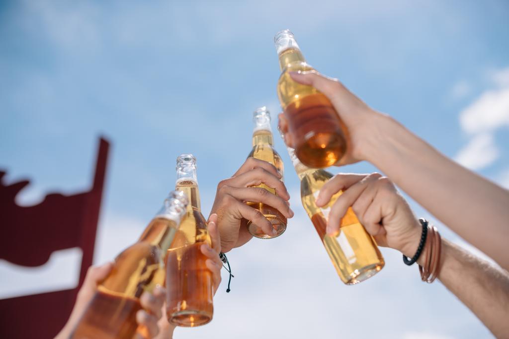 обрезанный снимок молодых людей, звенящих бутылки пива на открытом воздухе
  - Фото, изображение