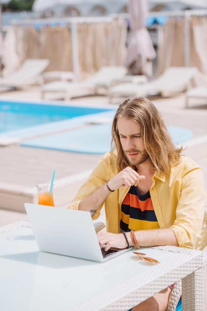 handsome young man drinking cocktail while sitting near pool - Photo, Image
