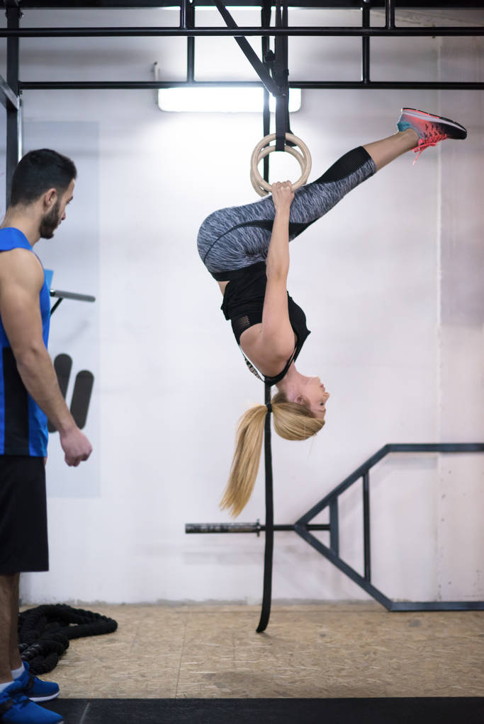 nuori urheilullinen nainen treenaa henkilökohtaisen kouluttajan kanssa voimistelurenkailla ristillä kuntosalilla - Valokuva, kuva
