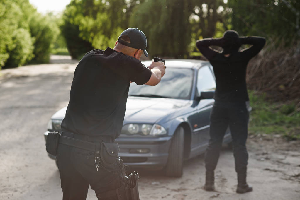 De politieman is gericht op de dader in de buurt van de gestolen auto. Stoppen van de criminaliteit. - Foto, afbeelding
