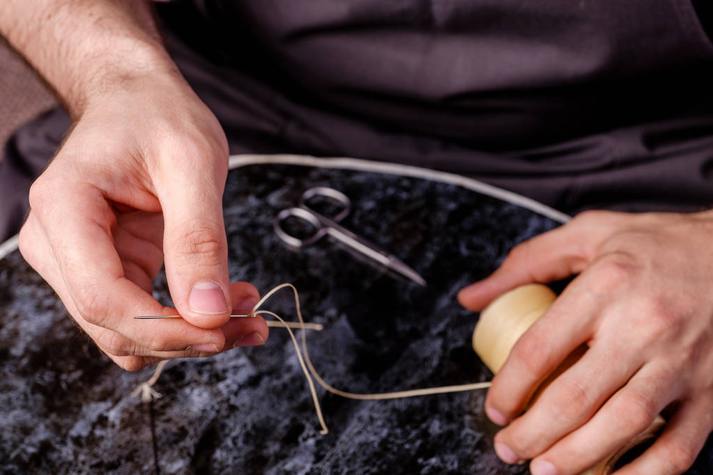 agulha de couro e linha encerada nas mãos dos homens, ferramentas usadas por sapateiros
 - Foto, Imagem