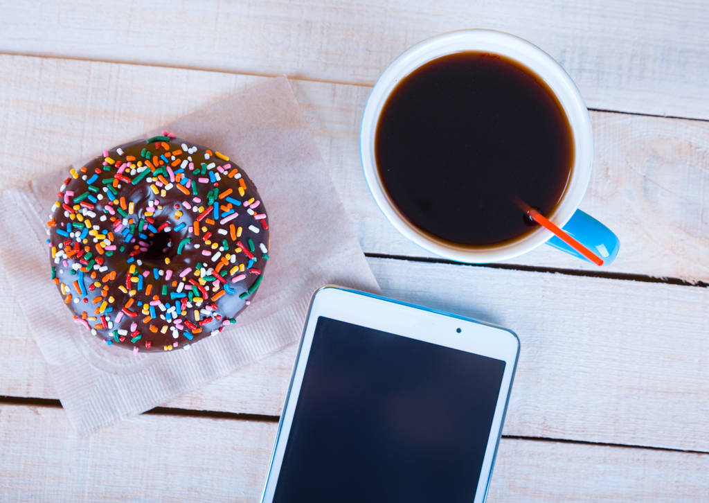 Schokoladen-Donut mit Streusel und Kaffee und einem Tablet über Kopf erschossen - Foto, Bild