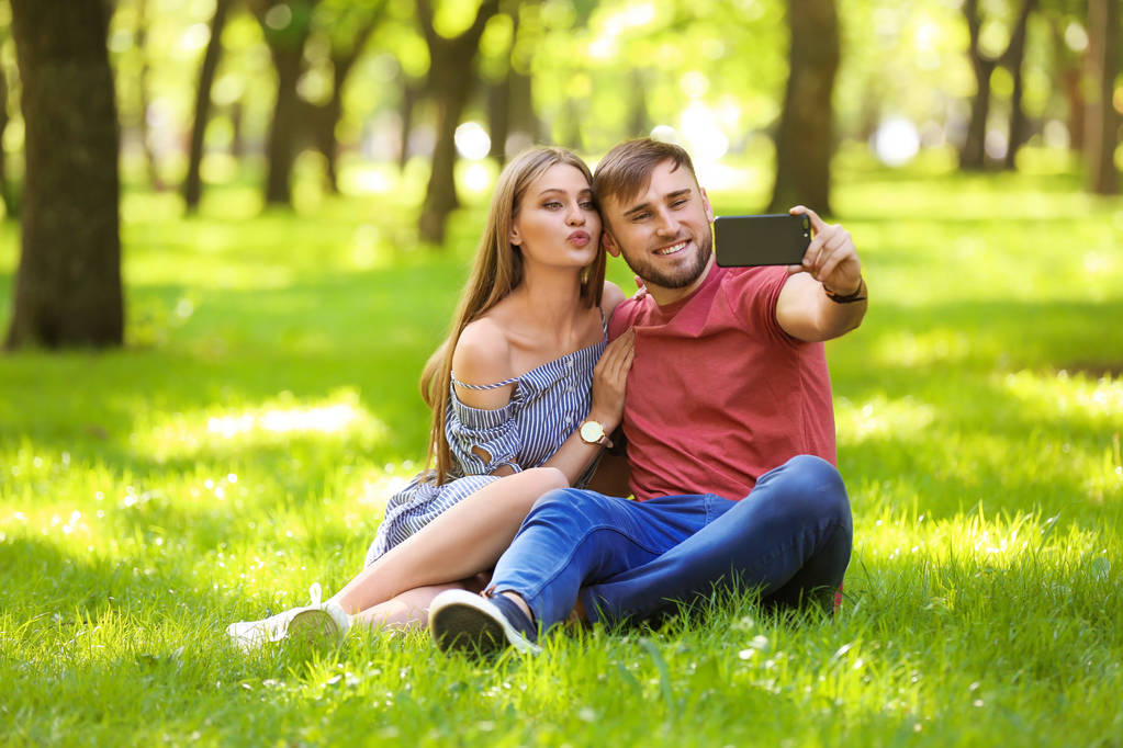 Boldog fiatal pár figyelembe selfie a zöld gyep a parkban - Fotó, kép