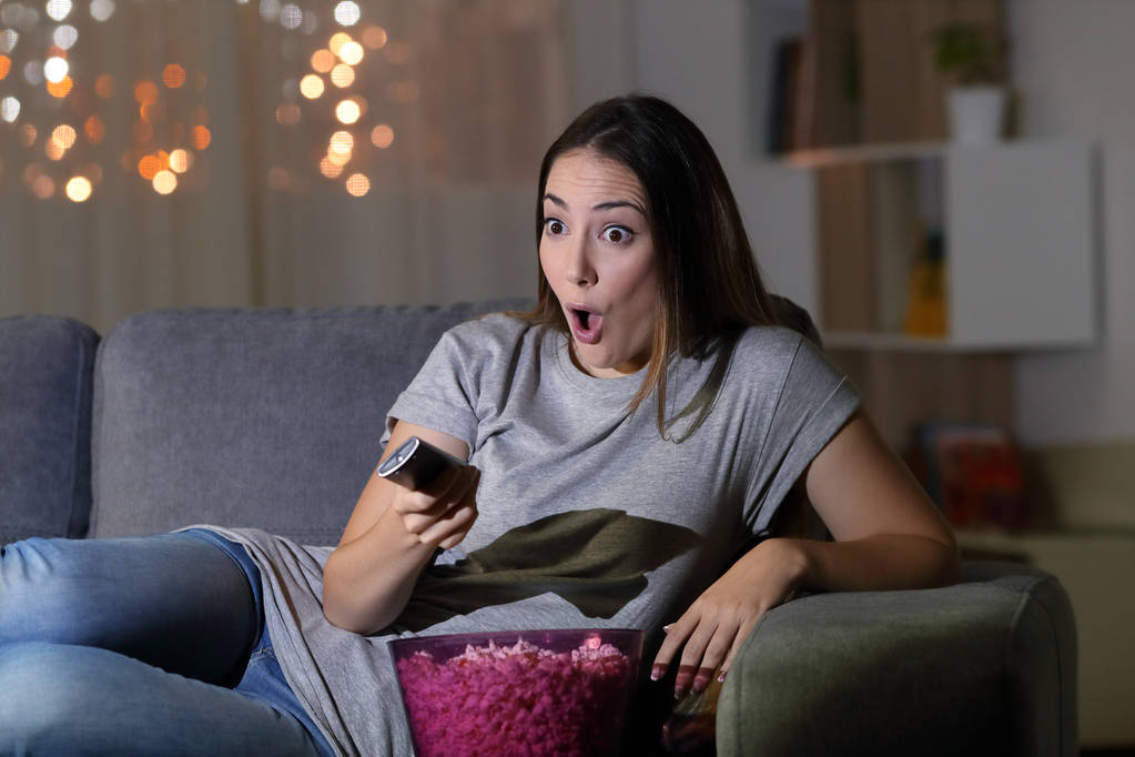 Hämmästynyt nainen katsomassa televisiota yöllä istuu sohvalla olohuoneessa kotona
 - Valokuva, kuva