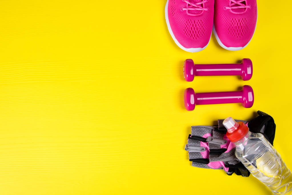 rosafarbene Turnschuhe und Fitnesszubehör sowie eine Flasche Wasser auf gelbem Hintergrund mit Platz zum Schreiben - Foto, Bild