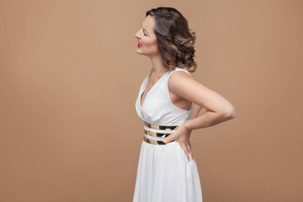 жінка в білій сукні, зворушлива назад, маючи біль у нирках на світло-коричневому фоні
 - Фото, зображення
