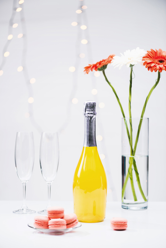vista de perto de macarons, copos vazios, garrafa de champanhe e buquê de flores de gerbera em fundo cinza
 - Foto, Imagem