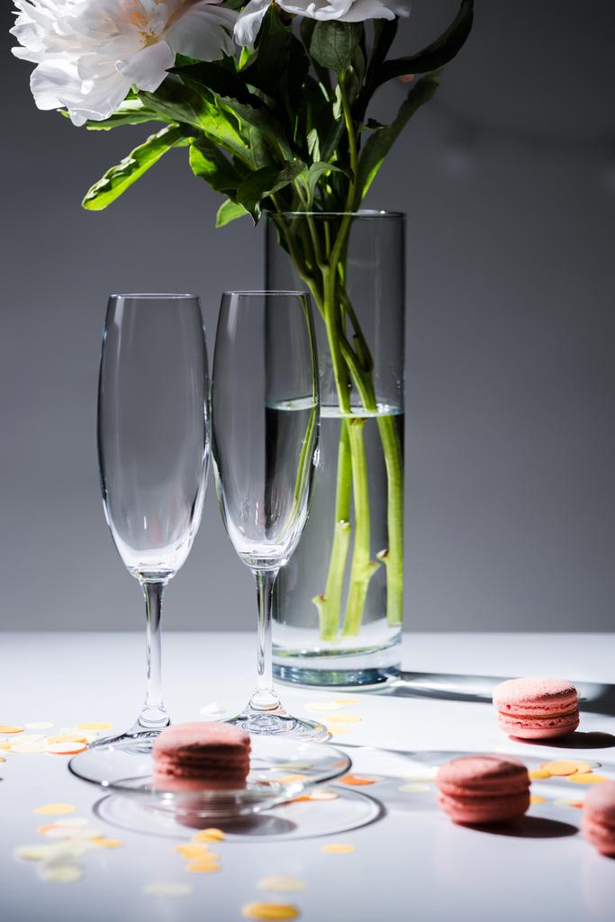 закрыть вид пустых стаканов, сладких макарон и букет цветов в вазе на сером фоне
 - Фото, изображение