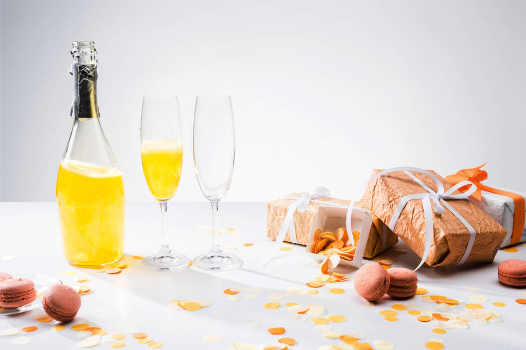 Close-up van glaswerk met gele champagne, macarons en gearrangeerd geschenken op grijze achtergrond - Foto, afbeelding
