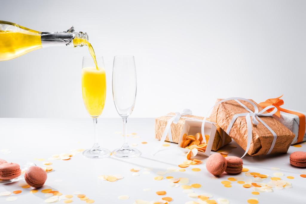 vista de perto de derramar champanhe amarelo no processo de vidro e presentes arranjados em pano de fundo cinza
 - Foto, Imagem