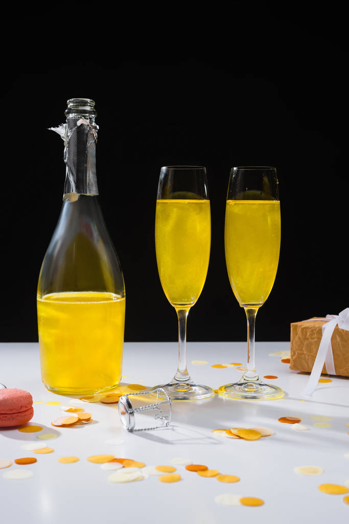 vue rapprochée de la bouteille et des verres de champagne jaune, macaron et cadeau à la surface sur fond noir
 - Photo, image