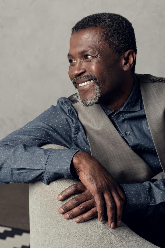 πορτρέτο του όμορφος μέσης ηλικίας αφρικανική αμερικανική άνδρα χαμογελώντας σε γιλέκο κάθεται στην πολυθρόνα - Φωτογραφία, εικόνα