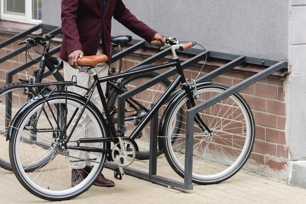 обрізаний вид на стильного чоловіка з велосипедом на парковці для велосипедів
 - Фото, зображення