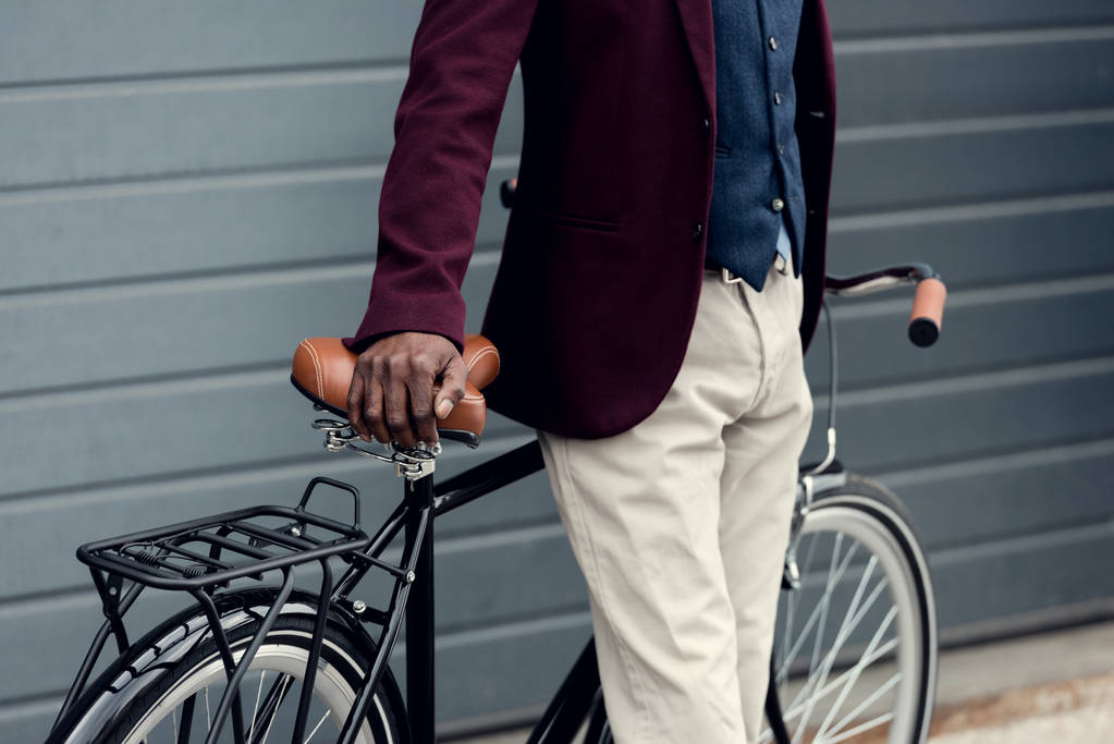 Ausgeschnittene Ansicht eines eleganten afrikanisch-amerikanischen Mannes, der sich auf ein Fahrrad stützt  - Foto, Bild