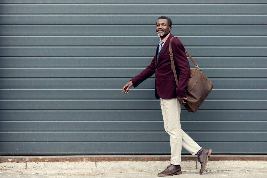 μοντέρνα αφρικανική αμερικανική άνθρωπος σε Βουργουνδία σακάκι με δερμάτινη τσάντα - Φωτογραφία, εικόνα