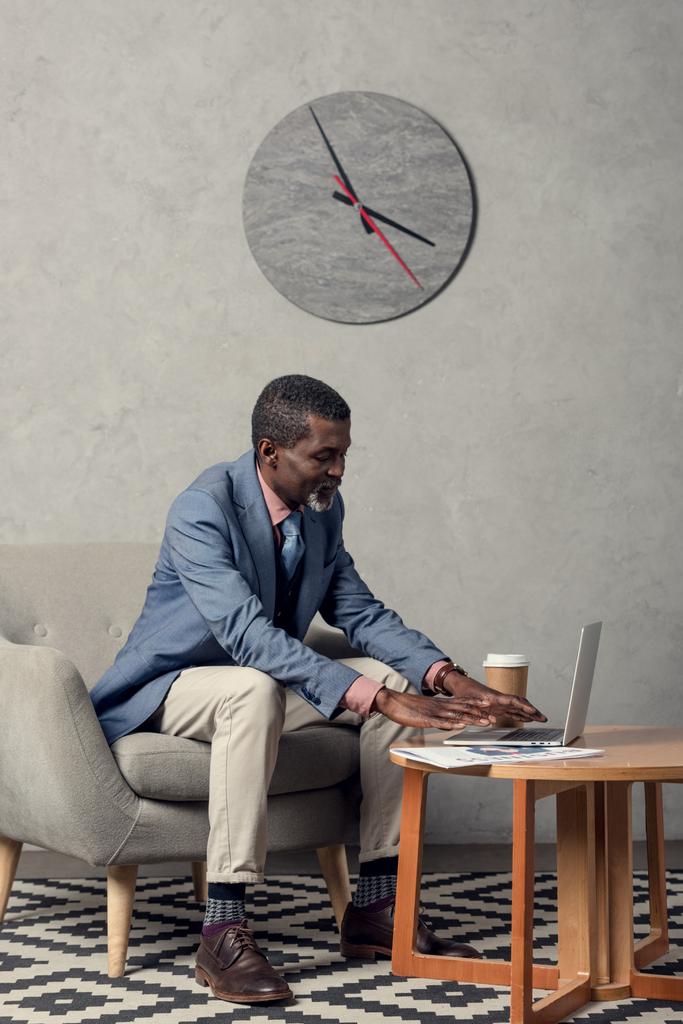 élégant homme d'affaires afro-américain d'âge moyen utilisant un ordinateur portable à table avec café et journal
 - Photo, image