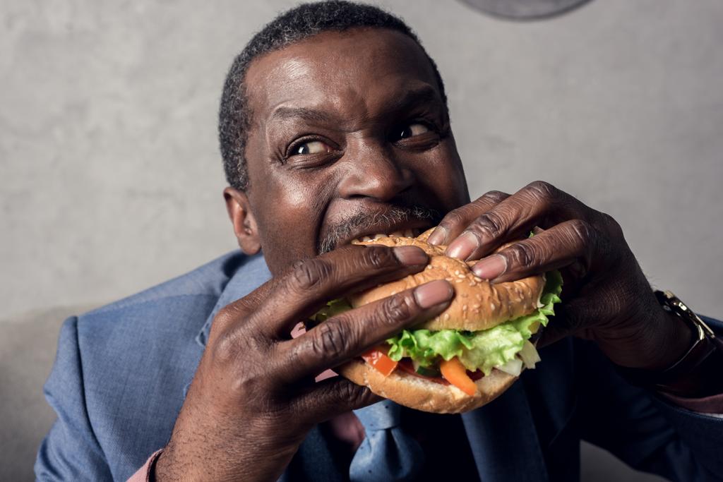 ハンバーガーを食べて空腹のアフリカ系アメリカ人のビジネスマン - 写真・画像