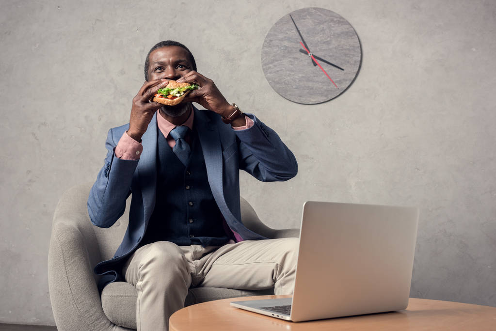 maturo uomo africano americano mangiare hamburger a tavola con computer portatile
 - Foto, immagini