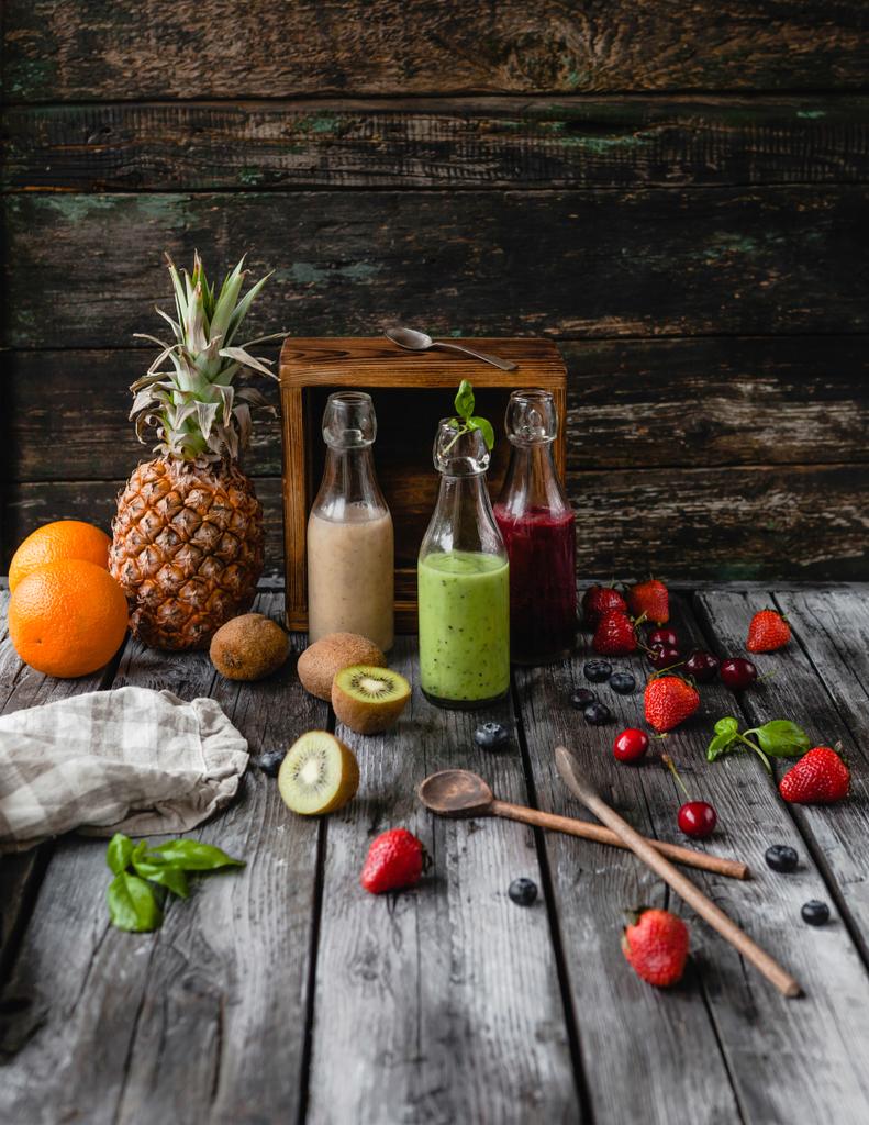 Delicious detox smoothies in glass bottles on rustic wooden board with assorted fruits - Photo, Image