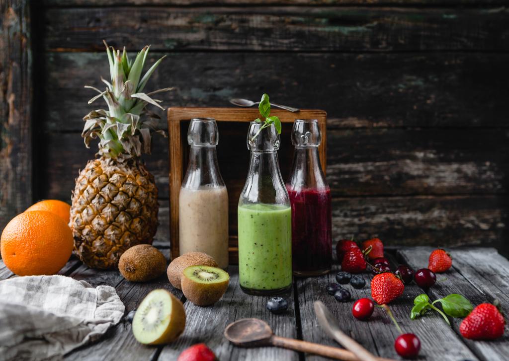 Bio-Frucht-Smoothies in Glasflaschen auf Holzgrund mit verschiedenen Früchten - Foto, Bild