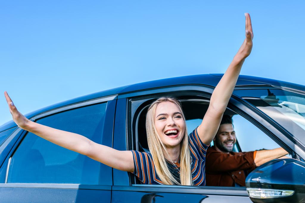 щаслива молода жінка з широкими руками, що виступає з вікна автомобіля, поки її хлопець водить машину
  - Фото, зображення