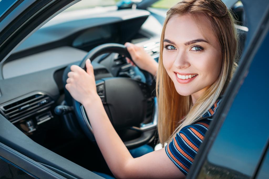 πορτρέτο του χαμογελώντας νεαρή γυναίκα που κάθεται πίσω από τιμόνι αυτοκινήτου  - Φωτογραφία, εικόνα