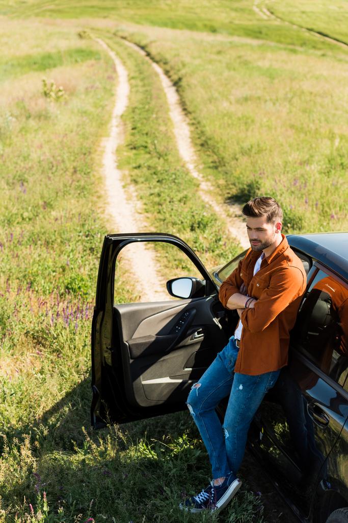 високий вид на молодого чоловіка з схрещеними руками, що стоять біля його машини в полі
  - Фото, зображення